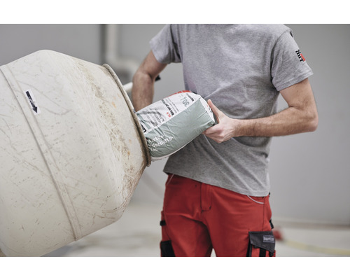 Mann schüttet eine Sack Zement in einen Betonmischer