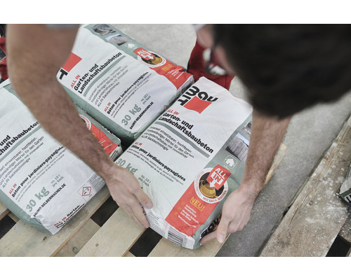 Person hantiert mit Säcken Baumit All in Garten- und Landschaftsbaubeton 30 Kilogramm auf einer Palette