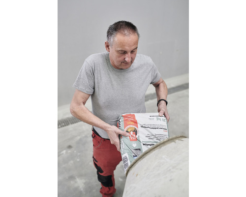 Ein Mann leert einen Sack Betonmischung in einen Mischer.