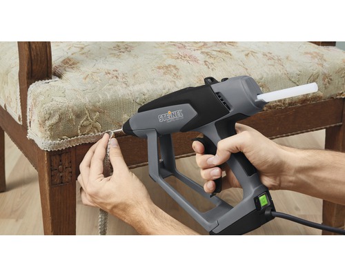 Une personne fixe une bordure sur une chaise avec un pistolet à colle chaude.