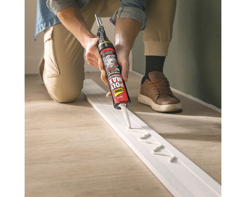 Eine Person trägt Klebstoff mit einer Klebepistole auf eine Fußleiste auf.