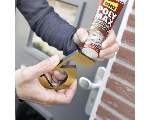 Eine Person befestigt eine goldfarbene Hausnummer mit Montagekleber.