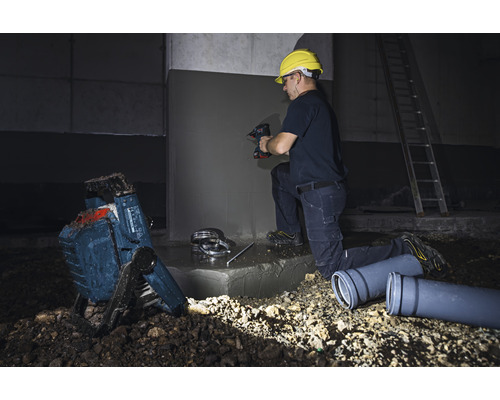 Artisan au travail avec une perceuse, un projecteur de chantier et des tuyaux d'évacuation sur un chantier