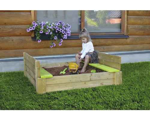 Enfant jouant dans un bac à sable avec des jouets dans le jardin