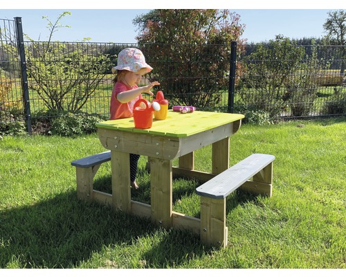 Un enfant joue à une table de pique-nique dans le jardin. La table en bois a des bancs et un plateau vert.