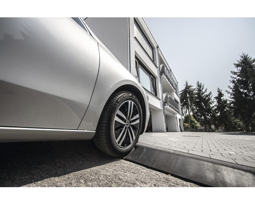 Une voiture avec un pneu Michelin est garée au bord de la route devant un bâtiment.