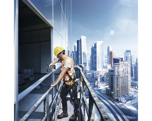 Un ouvrier du bâtiment portant un casque et un gilet de sécurité installe des fenêtres sur un bâtiment en hauteur