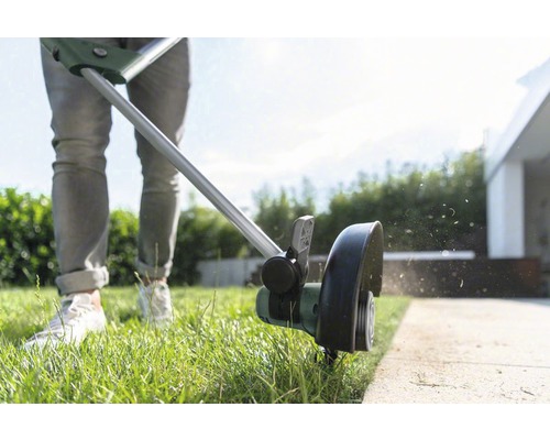 Une personne coupe les bordures de pelouse avec un coupe-bordure.
