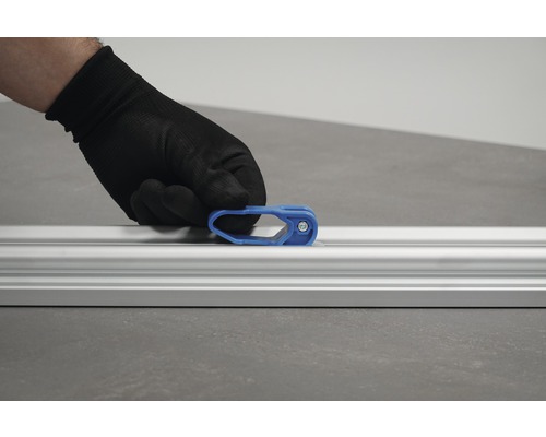 Une main avec un gant de protection fixe un curseur bleu sur un rail en aluminium.