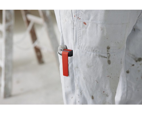 Eine Person trägt eine Latzhose mit Farbklecksen und einem Rollenhalter in der Tasche.