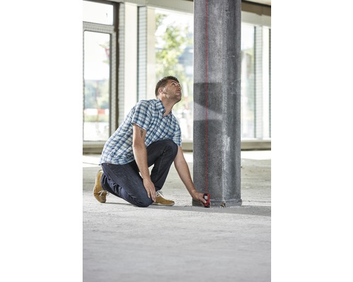 Mann benutzt einen Laser Entfernungsmesser an einem Betonpfeiler in einem Gebäude.