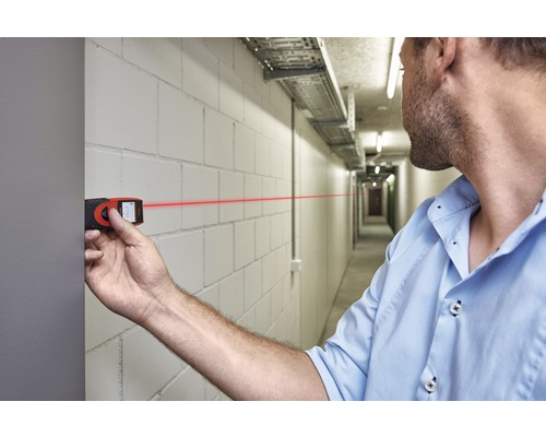 Mann misst mit Laser-Entfernungsmesser in einem Korridor