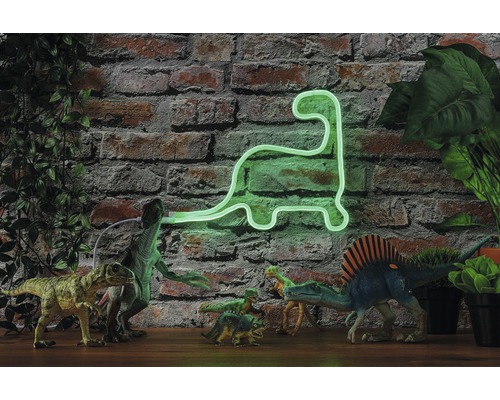Lumière néon décorative dinosaure devant un mur de briques, entourée de dinosaures jouets et de plantes.