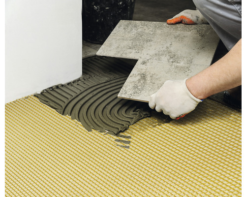 Un carreleur pose des carreaux de sol avec de la colle à carrelage et une natte de désolidarisation.