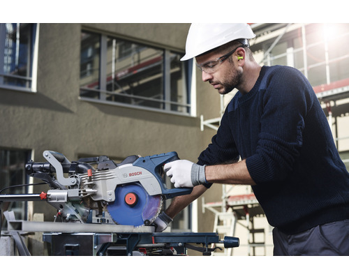 Un homme portant un casque et des lunettes de protection utilise une scie à onglet Bosch.