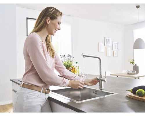 Une femme remplit un verre d''eau au niveau de l''évier de cuisine avec un robinet dans une cuisine lumineuse.