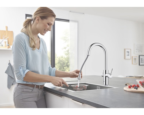 Femme rinçant des baies dans une passoire sous un robinet de cuisine avec douchette extractible.