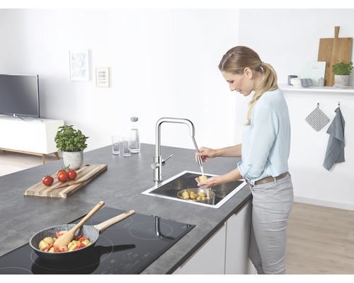 Femme lavant des pommes de terre dans un évier en acier inoxydable avec un robinet chromé dans une cuisine.