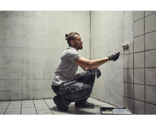 Homme peignant un mur carrelé avec un rouleau à peinture
