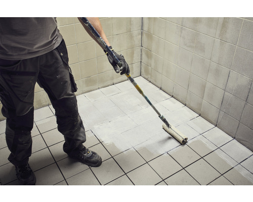 Artisan peint un carrelage avec un rouleau à peinture dans une salle de bain.