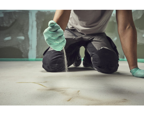 Un artisan applique une chape sur le sol