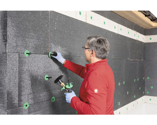 Un homme fixe des panneaux isolants à un mur à l''aide de chevilles d''isolation.