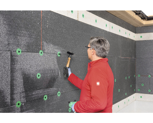 Un homme fixe des panneaux isolants au mur avec un marteau