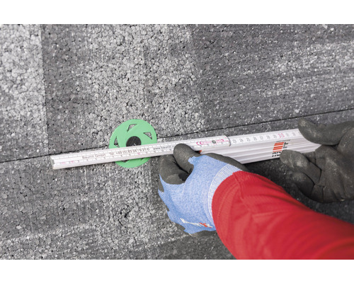 Une personne mesure l''isolation avec un mètre pliant et une rosace d''isolation.