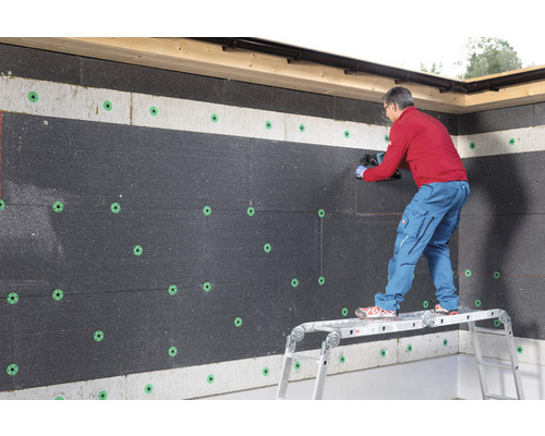 Un homme coupe des panneaux isolants sur un mur avec des chevilles d''isolation.