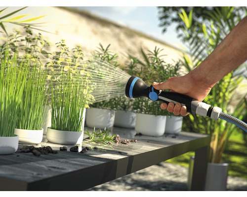 Eine Person bewässert Pflanzen in Töpfen mit einer Gartenspritze auf einem Tisch.