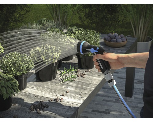 Hand bewässert Pflanzen mit einer Gartenspritze auf einem Tisch im Freien.