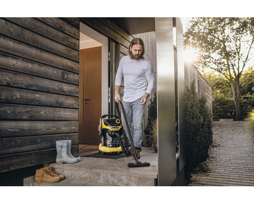 Un homme utilise un aspirateur eau et poussière Kärcher à l''extérieur d''une maison à bardage bois.