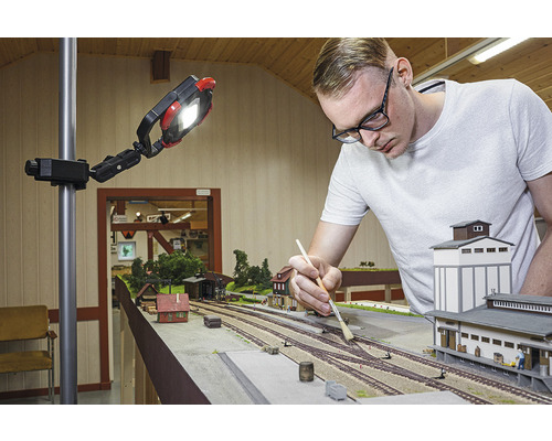 Mann arbeitet an einer Modelleisenbahn unter einer Arbeitsleuchte.
