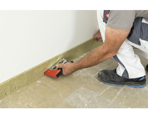 Un ouvrier fixe une plinthe à un mur avec une agrafeuse.