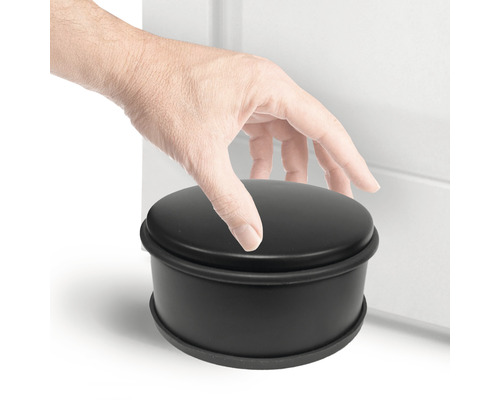 Butoir de porte rond noir à côté d''une porte avec une main dessus