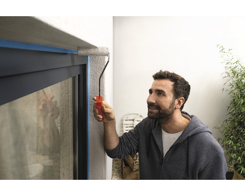 Un homme peint un cadre de fenêtre avec un rouleau à peinture, qui a été recouvert de ruban adhésif.