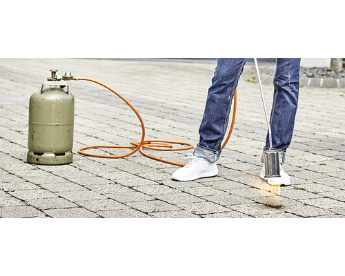 Personne utilisant un brûleur à gaz pour désherber sur des pavés, bouteille de gaz en arrière-plan
