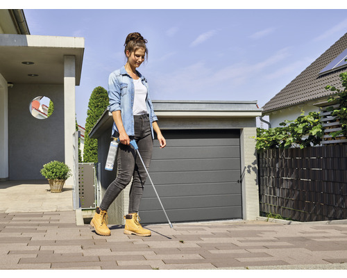 Eine Frau verwendet ein Unkrautbekämpfungsmittel auf einem Gehweg vor einer Garage.