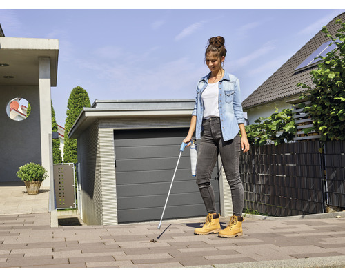 Frau benutzt einen Abfallsammler vor einem Haus mit Garage