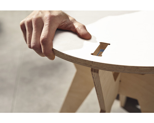 Gros plan d''un tabouret en contreplaqué avec une assise ronde, tenu par une main