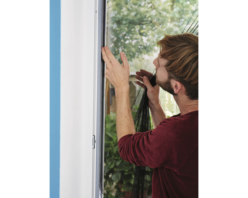 Un homme fixe une moustiquaire sur un cadre de fenêtre.