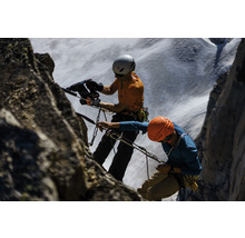 Zwei Bergsteiger mit Helmen und Seilen klettern an einem Felsen.