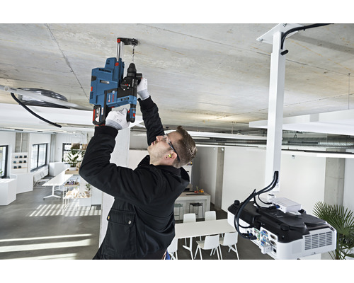 Un homme perce un trou dans le plafond d'un bureau avec une perceuse