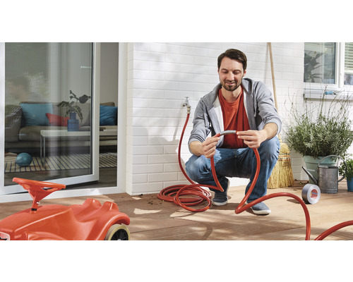 Mann schliesst einen roten Gartenschlauch an einen Wasserhahn auf einer Terrasse an