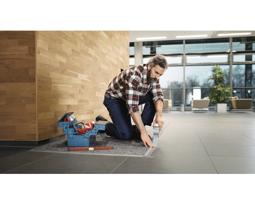 Handwerker mit Werkzeugkiste verlegt Bodenleisten in einem Gebäude