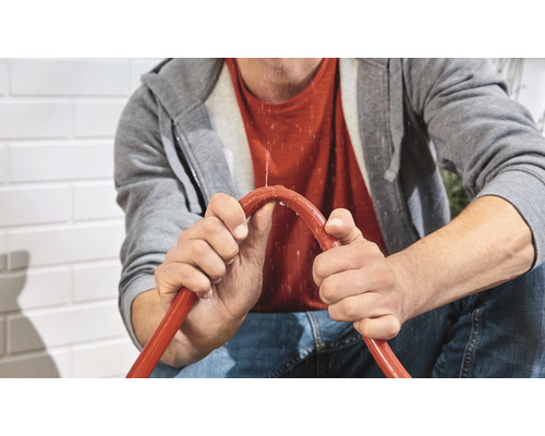 Mann hält einen undichten Gartenschlauch