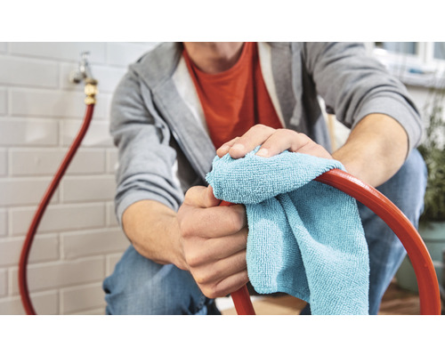 Mann reinigt einen Gartenschlauch mit einem Mikrofasertuch.