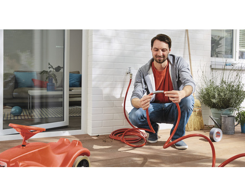 Homme réparant un tuyau d''arrosage sur une terrasse avec une voiture jouet