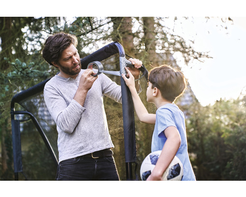 Vater und Sohn reparieren ein Fussballtor mit Klebeband im Garten.
