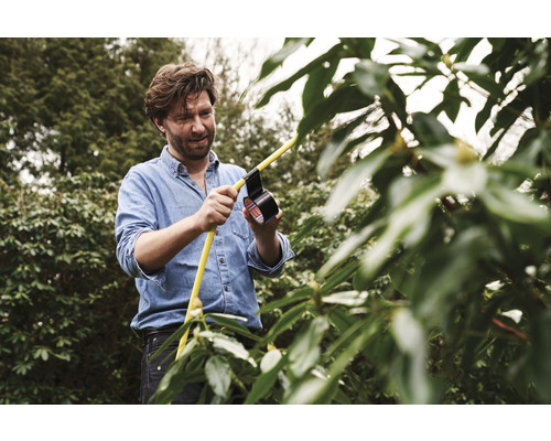Mann repariert einen gelben Gartenschlauch mit schwarzem Isolierband im Garten.